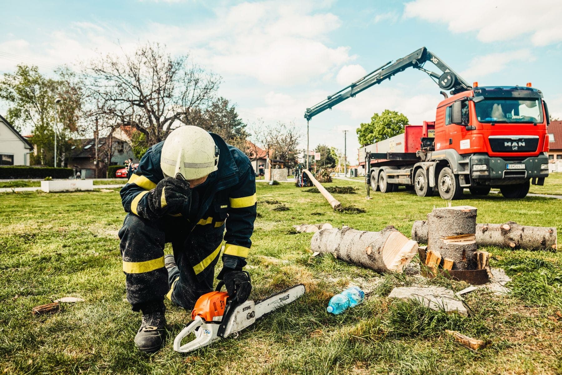 Pocięty pień drzewa na trawniku, w tle samochód z dźwigiem do załadunku
